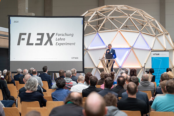 Ein Sprecher spricht vor sitzendem Publikum in einer Halle