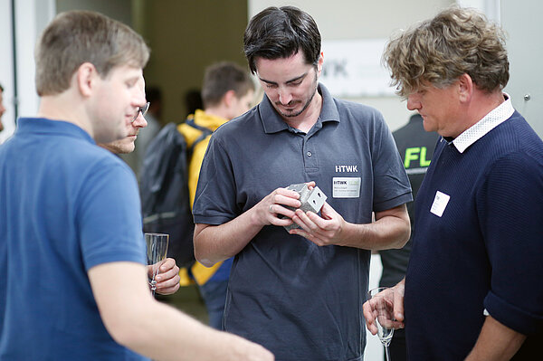 Drei Männer stehen am Informationsstand und begutachten einen Stahlwürfel